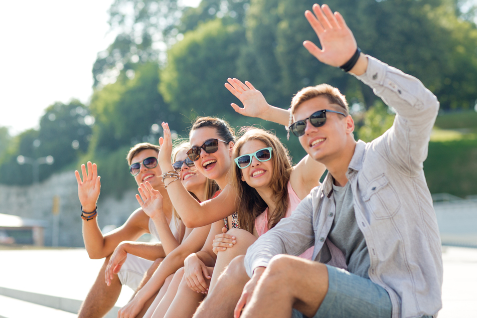 friendship, leisure, summer, gesture and people concept - group of smiling friends sitting on city square